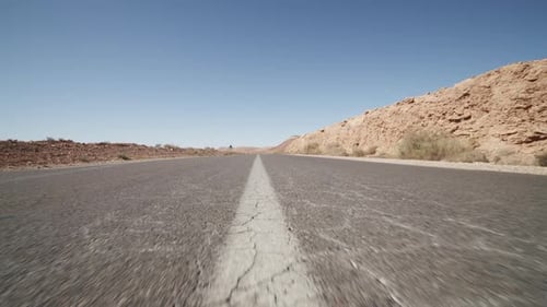 SLOW MOTION: LOW SHOT FLYING OVER ASPHALT STREET IN DESERT ON SUNNY DAY