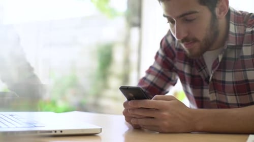 Young Man Looks at Phone at Desk
