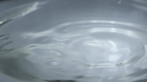 Wassertropfen fallen in Zeitlupen-Makroaufnahme auf die Wasseroberfläche