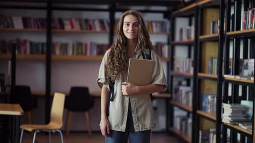 Portrait of Young Pretty Woman Smiling Happy Looking at Camera in Library Bookshelf Background