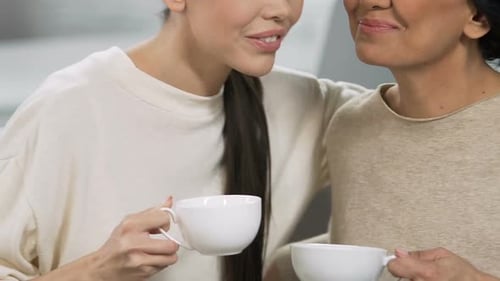 Hermanas adultas sonriendo y hablando con tazas de té, ambiente relajante en casa, apoyo