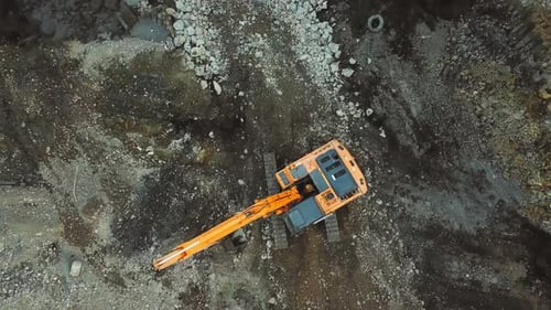 Large yellow excavator or bulldozer moves around construction site or quarry.