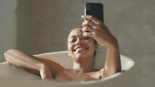 Woman Relaxing in Tub Taking Selfie with Phone