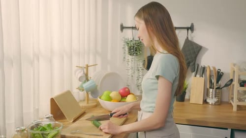 Young Caucasian attractive woman cook green salad in kitchen at home.