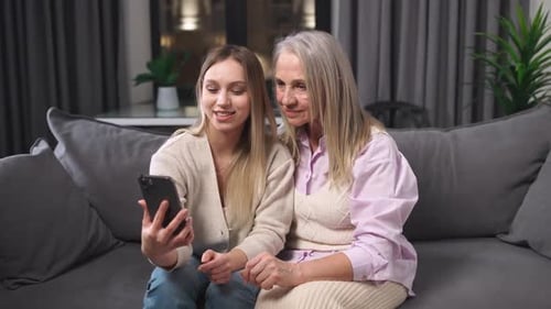 Granddaughter and Grandmother View Photos on a Smartphone Sitting in the Living Room Family Day