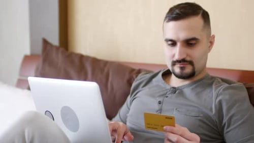 Man Uses Laptop and Bank Card Indoors