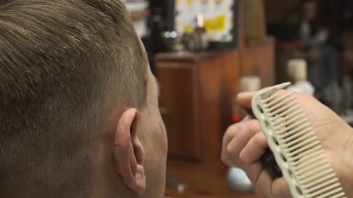 Nahaufnahme der Rückseite eines männlichen Friseurs, der einem männlichen Kunden ordentlich die Haare schneidet