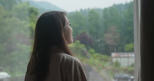 Woman Looking Out Window at Rainy Forest