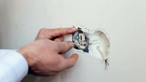 Hands Repairing Electrical Wiring with Screwdriver in Wall