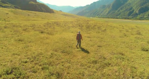 Flight Over Backpack Hiking Tourist Walking Across Green Mountain Field. Huge Rural Valley at Summer
