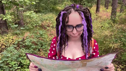 Traveling woman with dreadlocks with map in woods.