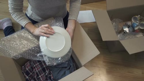 Woman Carefully Packing Dishes Into Cardboard Boxes