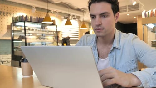 Young Man Working on Laptop in Cafe