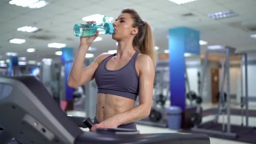 Young sporty Woman On Running Machine In Gym drinking water