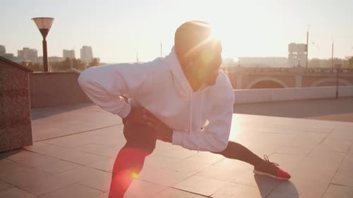 Muscular Man Stretching on Urban Plaza at Sunrise