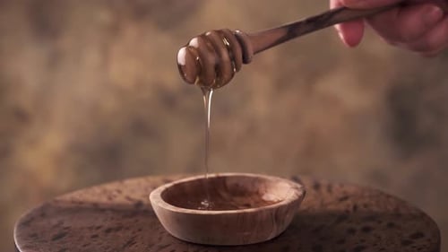Honey Dripping From Wooden Dipper into Bowl