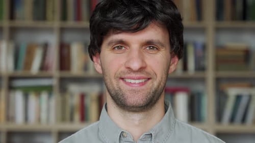 Man Student Standing in University Library and Looking Into Camera