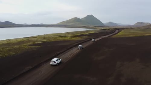 cars drive on a dirt road in the mountains