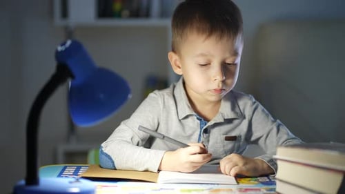 Boy Writes at Desk Under Blue Lamp