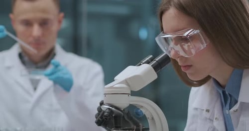 Woman Analyzing Sample Through Microscope in Bright Lab