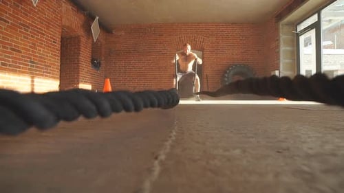 Young Caucasian Man Working Out with Battle Ropes at a Gym. Slow Motion