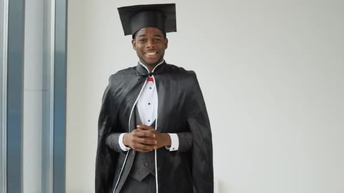 A Young Cheerful Graduate of African American Nationality Stands in Front of the Camera in a Black