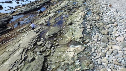 Tracking shot of a young man running on a rocky ocean beach shoreline
