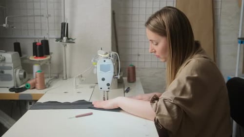 female tailor designer sews clothes, sitting in workshop at a table with a sewing machine