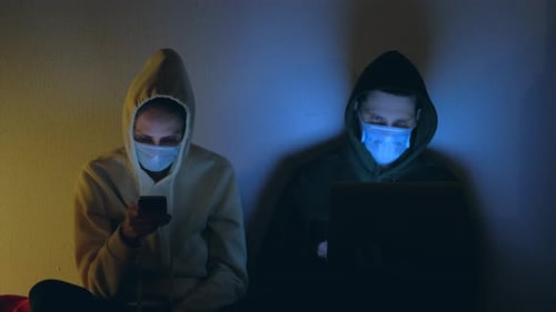 Two People in Hoodies with Devices at Night