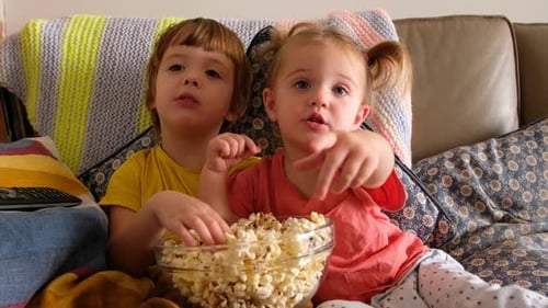 Children Eating Popcorn Together on Sofa at Home