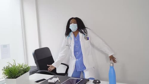Black female doctor in medical mask dancing in clinic