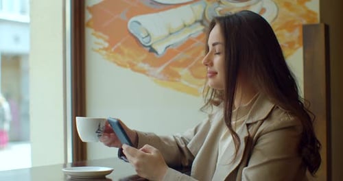 Young Woman Using Smartphone Drinking Coffee in Cafe Texting Sharing Messages on Social Media