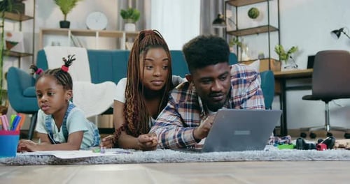Padres afroamericanos usan una computadora portátil mientras su hija dibuja