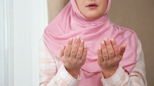 Unerkennbare Frau in rosa Hijab liest ein Gebet, während sie Händchen vor sich hält
