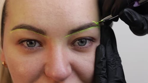 Die Hand eines Visagisten in schwarzen Handschuhen trägt eine gelbe Augenbrauenpaste auf die Augenbraue auf