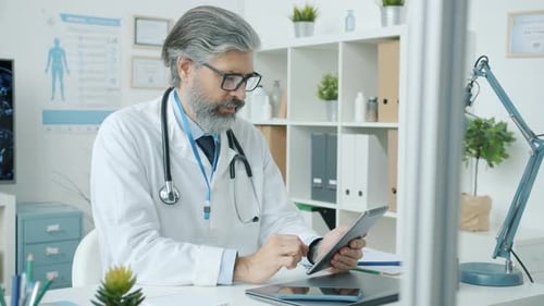 Portrait of Physician in White Coat Using Tablet Working in Office Room