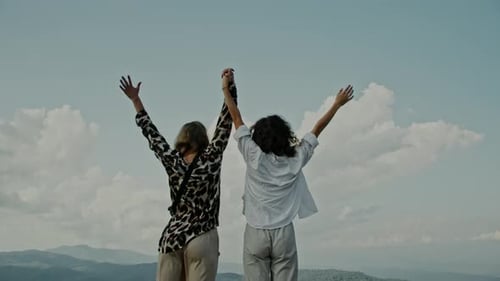 Slow Motion Closeup of Two Young Women Standing on the Edge of a Cliff and Raising Their Hands Up
