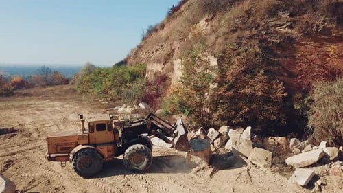 specially machinery with a bucket for picking stones is working in a quarry near the hill
