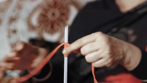 Woman starting first row of knitting with red wool and two needle crafts. Close up of knit work tie-