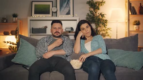 Husband and Wife Watching TV at Home and Eating Popcorn Late at Night Together