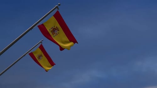 Waving Spain Flag on Pole Against Blue Sky
