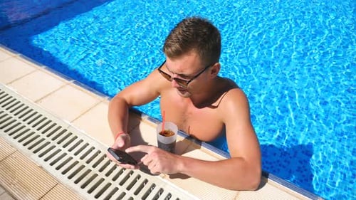Handsome Man Using Phone at Pool of Hotel and Refreshing Cold Cocktail