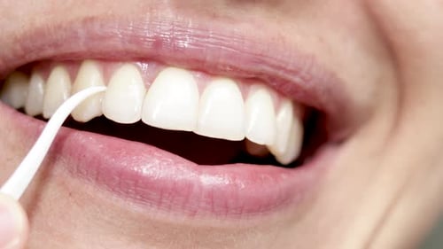 Nahaufnahme des Frauenmundes, reinigen Sie den Zahnzwischenraum und verwenden Sie Zahnseide mit einem Plastikzahnstocher. Lächelndes Mädchen mit