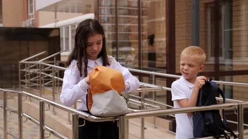 Small Schoolchildren Stand Near the School Entrance with Backpacks