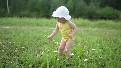 Little Funny Cute Blonde Girl Child Toddler in Yellow Bodysuit and White Hat Walking in Field with