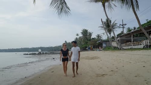 Honeymoon Interracial Couple Walking Holding Hands at a Tropical Island Beach at Sunset Front View