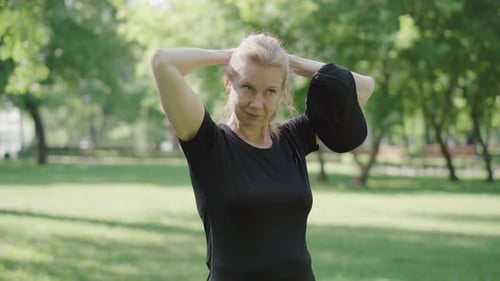 Woman Stretches and Puts on a Hat in Park