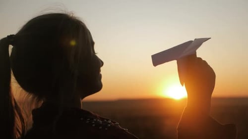 Child Holding Paper Airplane at Sunset