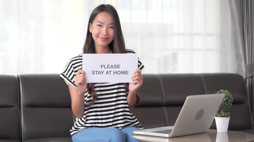 Smiling Woman on Sofa Holds Stay At Home Sign