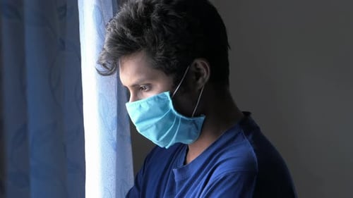 Um jovem com máscara protetora olhando pela janela